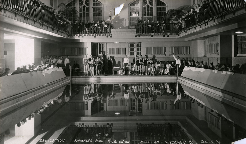 Photograph. Athletes in bathing suits stand at one end of pool; two prepare to jump in. Spectators sit along either side and in balcony above. Caption includes score "Mich. 49 - Wisconsin 20."